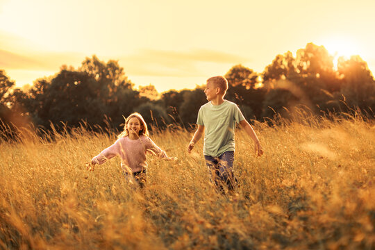 Happy Brother and Sister Running Together Through Golden Meadow at Sunset
