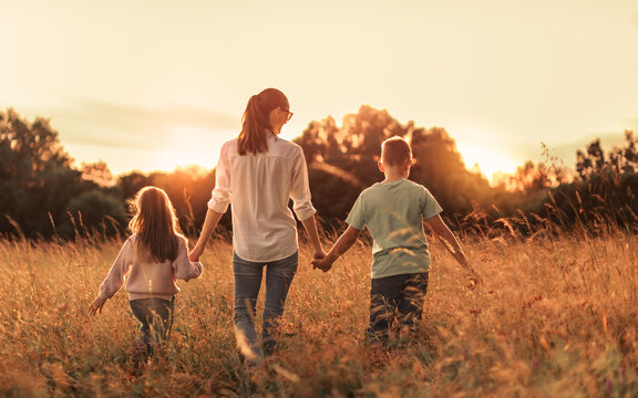 Mother Walking Hand in Hand With Two Children Through Golden Meadow at Sunset