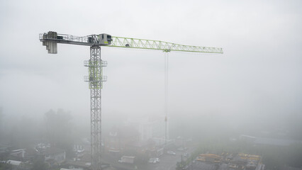 Naklejka premium Tower crane at a construction site covered in heavy fog. Urban building development in misty weather. Copy space for text