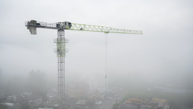 Tower crane at a construction site covered in heavy fog. Urban building development in misty weather. Copy space for text