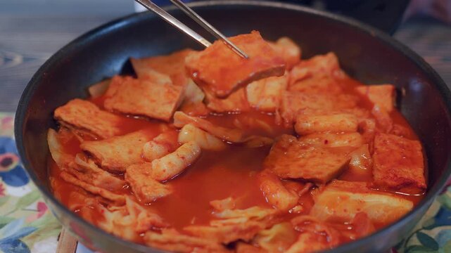 Close-Up of Chopsticks Picking Up Spicy Korean Rice Cake (Tteokbokki).
Close-up video of chopsticks picking up Tteokbokki (Spicy Korean Rice Cake) and fish cake in a pan. Delicious K-food cooking, str