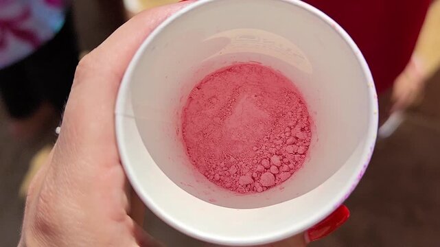 Hand holding cup of vibrant pink powder at outdoor event