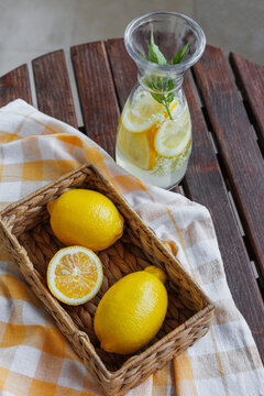 Top view of fresh lemons in a basket beside a glass carafe with lemon slices and mint, ideal for summer drink, detox water and wellness themes