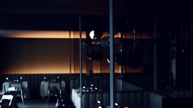 Tables are set with silverware and plates in a modern restaurant. The room is dimly lit and features a stylish design. It is evening and guests may arrive soon for dinner.