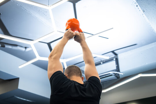 A muscular male trainer lifts a kettlebell in a gym