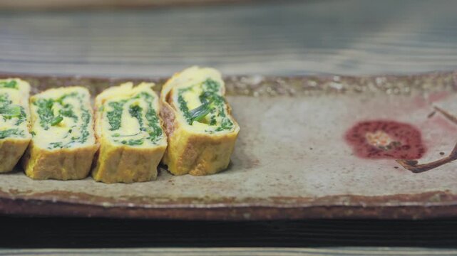 Close-up shot of hands arranging freshly sliced Korean rolled omelette (Gyeran-mari) onto a vintage ceramic plate.