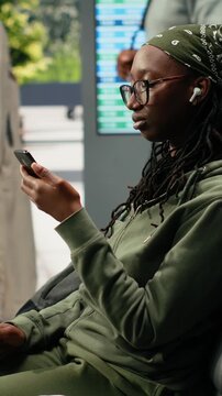 Vertical video: Traveler dictates a voice message on a smartphone in a bus terminal, holding the mobile phone near her mouth in the coach terminal while recording an audio message before departure.