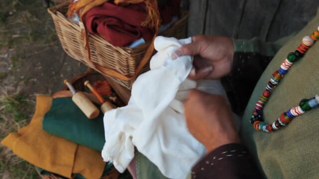Hands of medieval reenactor in period costume hand sewing linen fabric, close-up historical craft