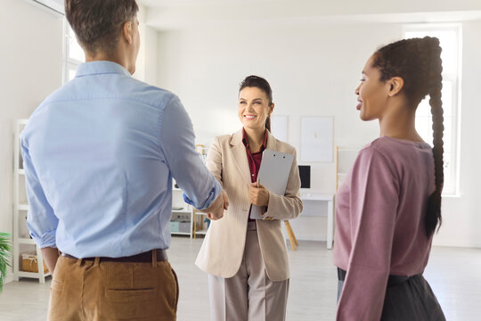 Agent and couple handshake at property. Smiling realtor meets clients in a flat during a consultation meeting, discussing rental agreement and contract details. Trust and deal theme shown.
