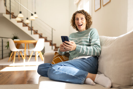 Woman reacting with surprise using smartphone on sofa