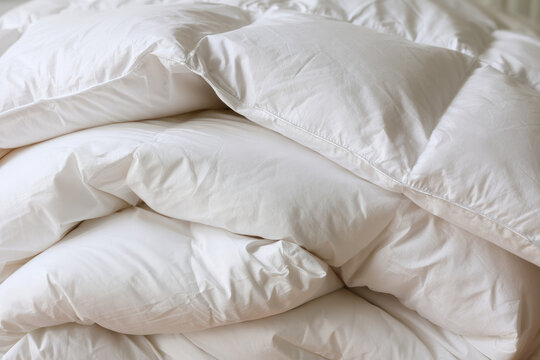 White down comforter, folded bedding, soft pillow pile creating cozy bedroom textile scene with quilted fabric texture, clean home interior styling, shallow focus and gentle natural light