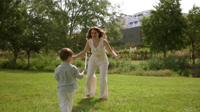 Playful mother and son blowing soap bubbles in the park