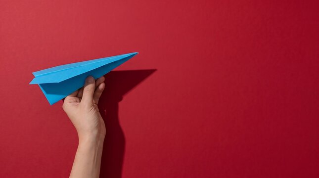 Hand Holding Blue Paper Airplane Over Red Background