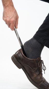 Using a shoehorn to put on a brown leather dress shoe with a grey sock