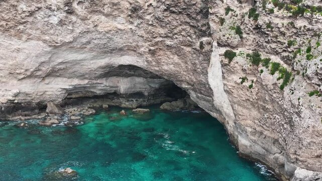 close aerial view limestone sea cave arch xaqqa cliffs malta overhanging rock ceiling turquoise water below eroded cliff face rugged texture mediterranean coastline overcast light