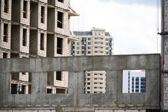 Unfinished concrete building structure during urban development with modern buildings visible in the background. Construction progress showing architectural transformation, structural work and city gr