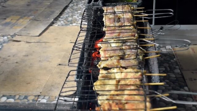 High angle view of traditional Asian seafood grilling over smoky hot embers, featuring seasoned fish fillet skewers being prepared with authentic culinary techniques at a busy market.
