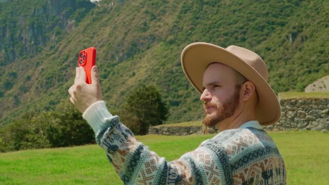 Adult man traveler taking a vertical selfie video with smartphone in mountain landscape, travel blog concept