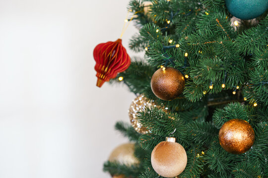 Close up golden Christmas ball hangs on spruce branch with illumination. Christmas tree ornaments in gold, teal, and soft beige tones, surrounded by glowing holiday lights background