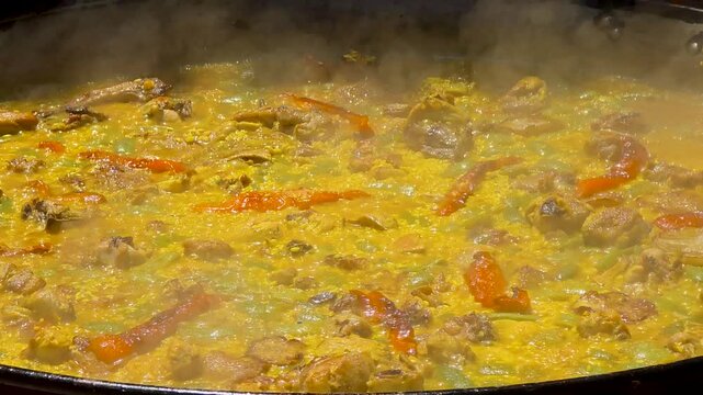 Close up of traditional Spanish paella boiling in large pan during cooking contest in slow motion.