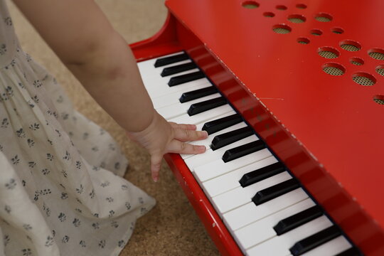 ピアノのおもちゃを手で触る子供。赤いキーボード。幼児の手