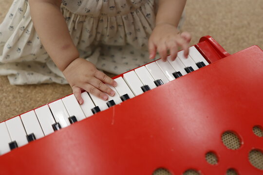 ピアノのおもちゃを手で触る子供。赤いキーボード。幼児の手