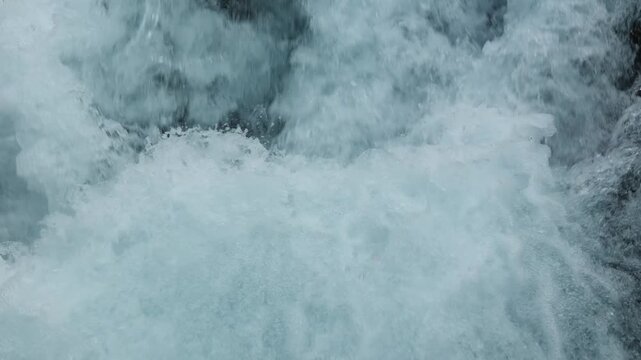 Close up of fast flowing water with white foam and clear aqua blue splash in a mountain stream