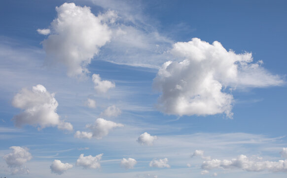 Bright blue sky filled with fluffy cumulus and delicate cirrus clouds. Natural atmospheric background with open space for travel, weather and conceptual designs.