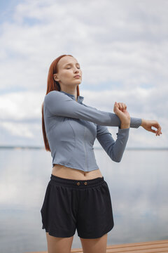 Young woman stretching outdoors near the waterfront before a workout. Fitness, running, wellness and active lifestyle concept.