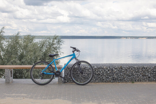 Blue bicycle parked beside a waterfront promenade under a cloudy sky. Outdoor recreation, travel and active lifestyle concept.