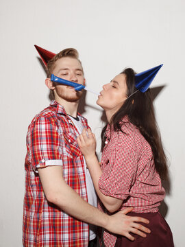 Young couple wearing colorful party hats celebrating together in a playful studio portrait. Birthday, celebration, romance and happiness concept.
