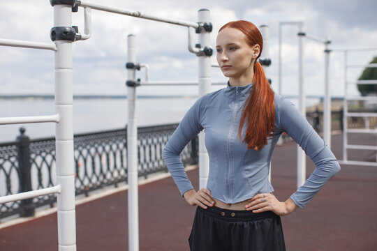 Young woman standing confidently on a waterfront promenade after exercising. Outdoor fitness, wellness and active lifestyle concept.
