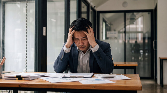 Stressed businessman office desk business man office stress anxiety headache paperwork document meeting room manager asian man suit tired overwhelmed work deadline failure problem office interior