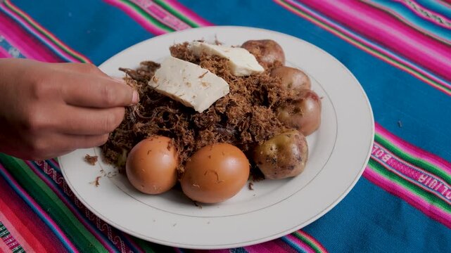 Bolivian dish called charquekan, featuring shredded llama meat, eggs, and potatoes, with a woman's hand in the frame - food concept