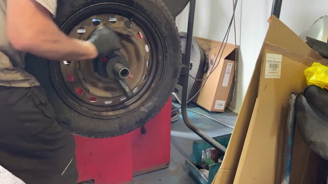 Close-up of a spinning car wheel mounted on a red balancing machine inside a garage. High-speed rotation during tire diagnostics or alignment process. Realistic auto service workshop environment.