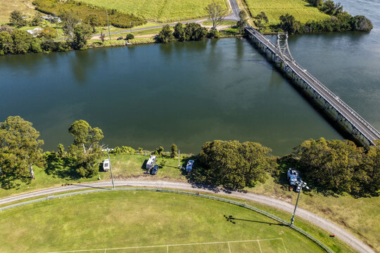 Aerial view of caravans set up alongside the Clarence River at Maclean Showground, featuring riverside camping, the broad waterway and the bridge visible in the background at Maclean 