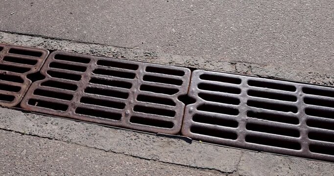 Brown metal storm drain grate on asphalt, old drainage grate is installed along the edge of a city road, urban environment