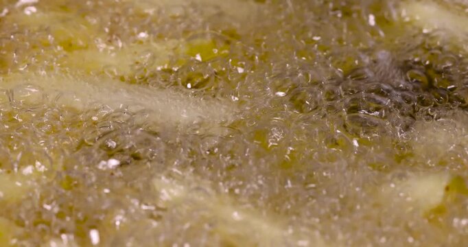 Yellow french fries potato sticks boiling in hot oil, cut raw french fries frying in greasy liquid fat with many small bubbles