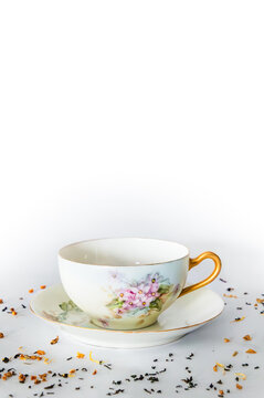 Empty teacup on saucer, tea leaves in foreground, white background, copy space above