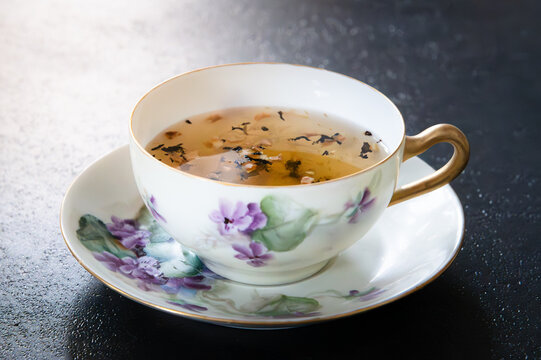 Teacup and saucer painted with purple lilac flowers, dark background
