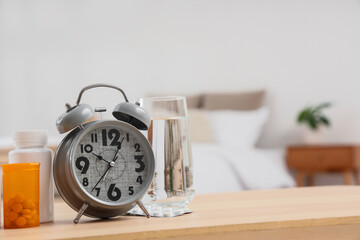 Naklejka premium Alarm clock with pill bottles and glass of water on table in bedroom