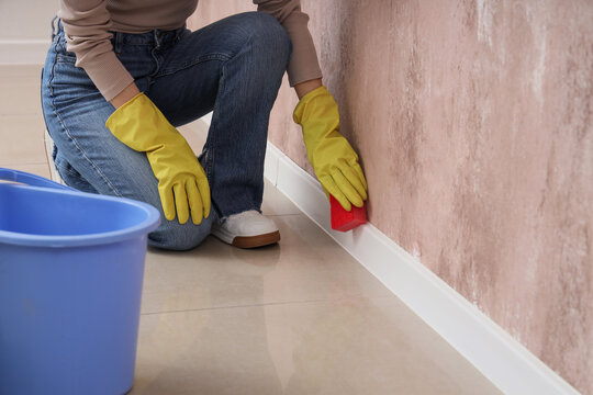 Woman with sponge cleaning white baseboard on grunge wall in room