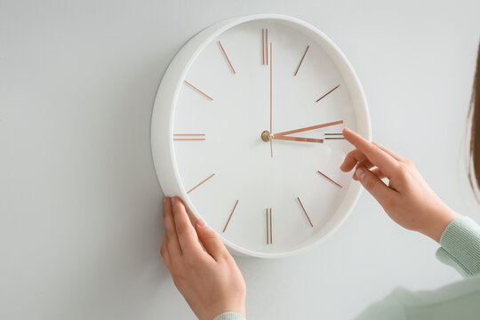Woman setting time on wall clock at home, closeup. Daylight saving time concept
