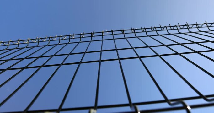 Black metal fence against a clear sky background, welded mesh grid of steel fence is installed against clean blue sky on a sunny day, private property