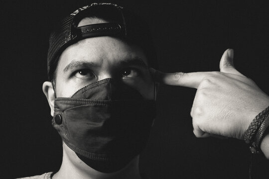 Man in face mask and backwards cap pointing finger gun gesture, black and white portrait with dramatic low key lighting