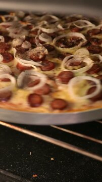 POV (slow zoom out): pizza maker checking the pizza inside the oven. Chef rotates the pizza with a spoon. Close-up: Pepperoni, mozzarella, and onion pizza baking in the oven. Pizzaiolo making pizza 