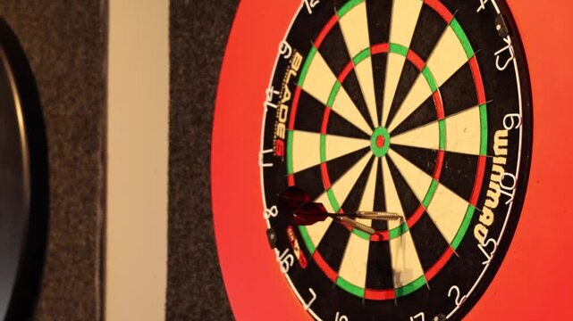 Three darts land in bullseye section of dartboard during game of darts.