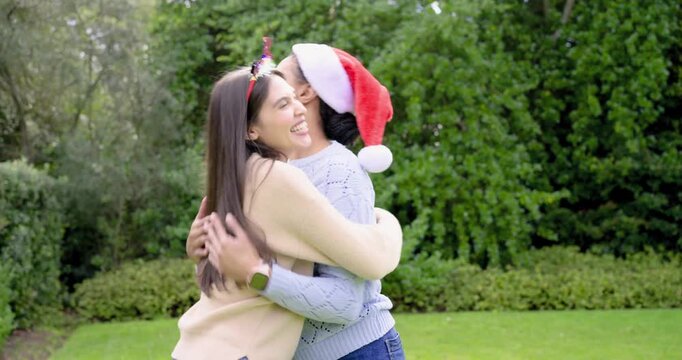 Female friends hugging and pointing on lawn on entry with Santa hat and headband, gazing off-screen