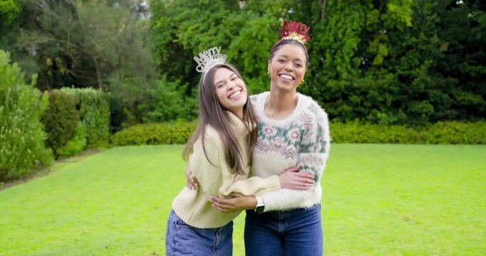 Smiling at camera Hispanic and African American women friends in sweaters hugging, laughing in yard