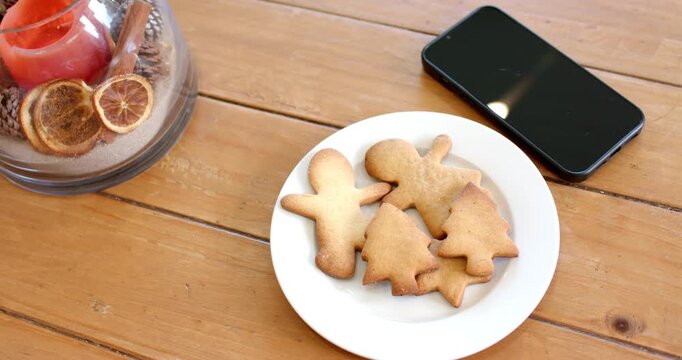 Camera hovering overhead, plate with gingerbread cookies center, bowl with candle left, phone right